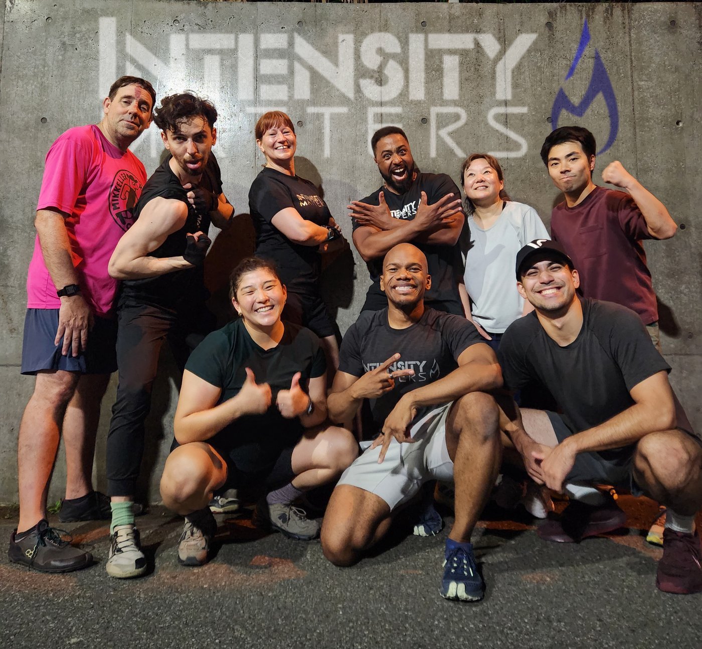 The Intensity Matters crew in front of the IM logo on the wall after class